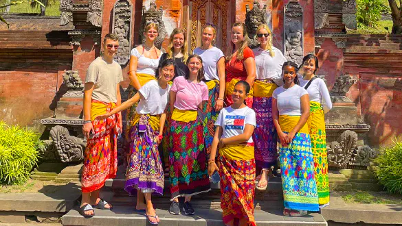 A group on vacation in Bali smiling as they dress in local Indonesian dress at a temple.
