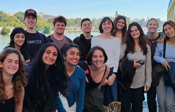 A group of smiling women and children stand together in colorful attire, conveying joy and community in front of a building with an open door.