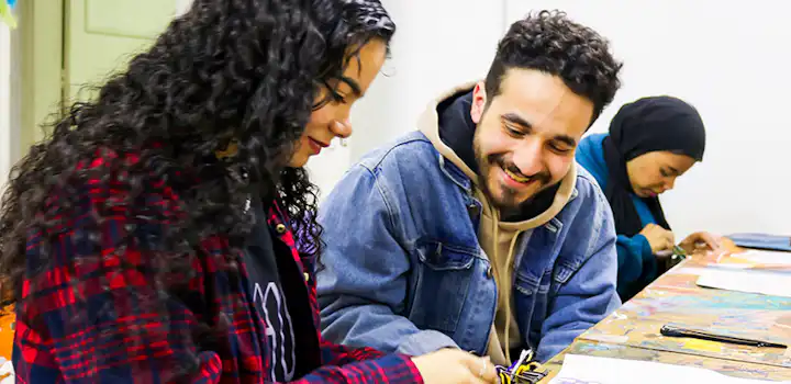 Participants smile and focus as they work on colorful embroidery patterns during a handicrafts session, part of IVHQ’s Women’s Empowerment project in Cairo, Egypt.