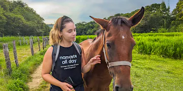 A female volunteer stands with a brown horse in a lush green field surrounded by trees in San José Manialtepec, Mexico.