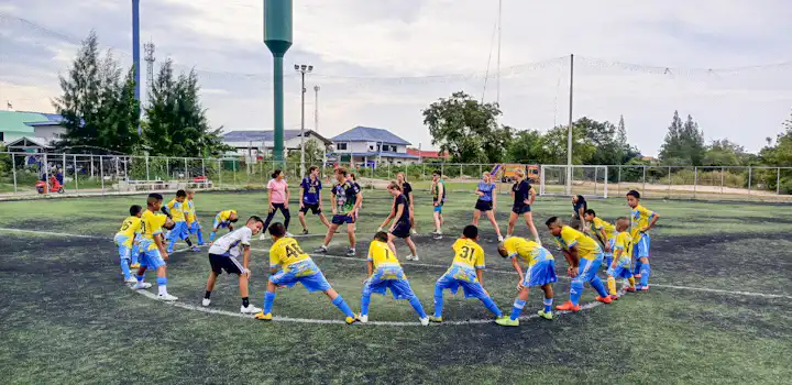 IVHQ volunteers are leading and guiding the local Thai children with the warm up to participate in a sports activity on a soccer field.